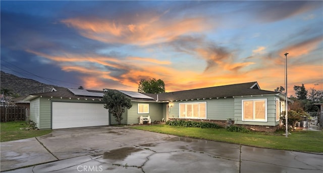 ranch-style home featuring fence, concrete driveway, a garage, a lawn, and roof mounted solar panels