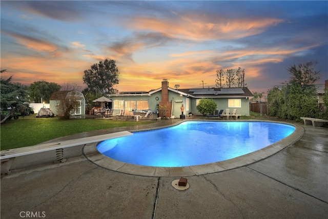 pool at dusk with a fenced in pool, fence, a lawn, a patio area, and a diving board