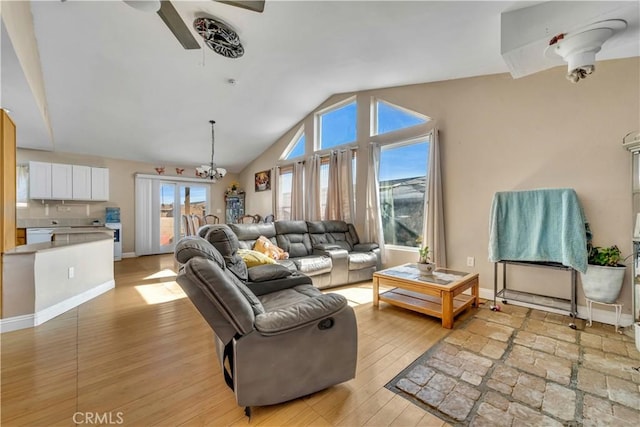 living area featuring ceiling fan with notable chandelier, lofted ceiling, light wood-style flooring, and baseboards