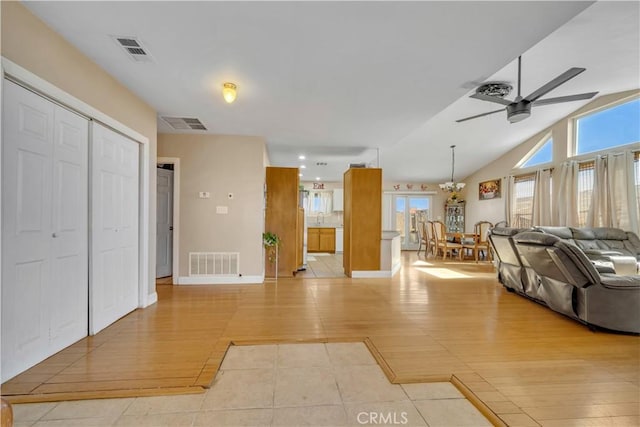 living area with lofted ceiling, visible vents, light wood finished floors, and ceiling fan with notable chandelier