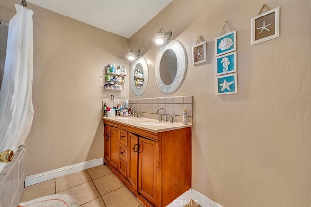 full bath featuring a sink, baseboards, tile patterned floors, double vanity, and tasteful backsplash