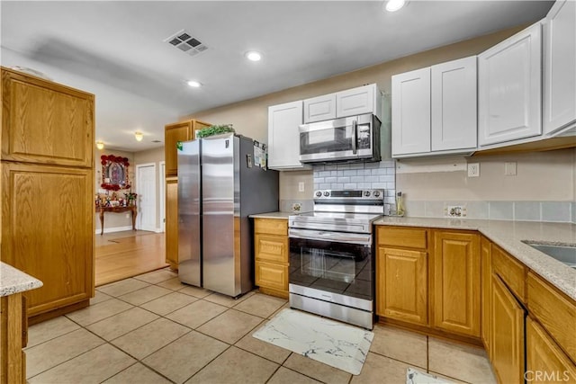 kitchen with light tile patterned floors, tasteful backsplash, visible vents, white cabinets, and stainless steel appliances