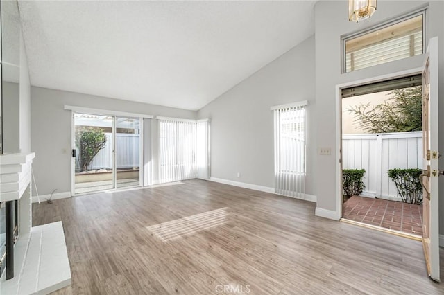 unfurnished living room with high vaulted ceiling, a fireplace, wood finished floors, and baseboards