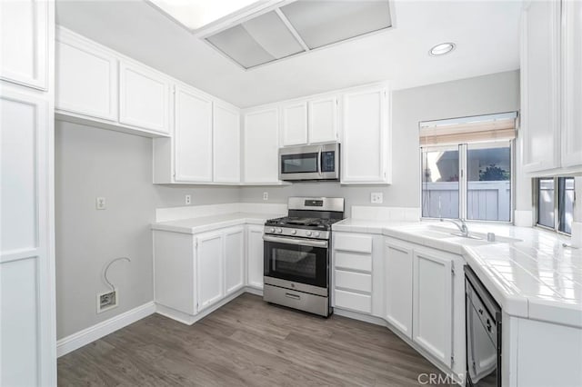 kitchen with tile counters, white cabinets, wood finished floors, stainless steel appliances, and a sink