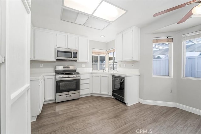 kitchen with light wood finished floors, baseboards, white cabinets, stainless steel appliances, and light countertops