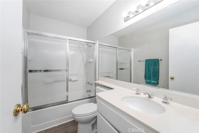 bathroom featuring toilet, enclosed tub / shower combo, wood finished floors, and vanity