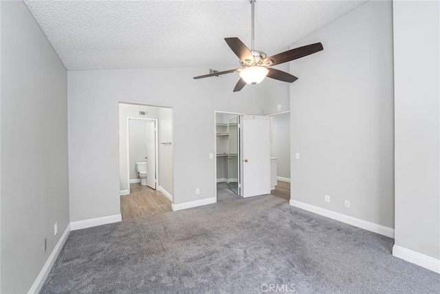 unfurnished bedroom with lofted ceiling, a textured ceiling, carpet flooring, and a walk in closet