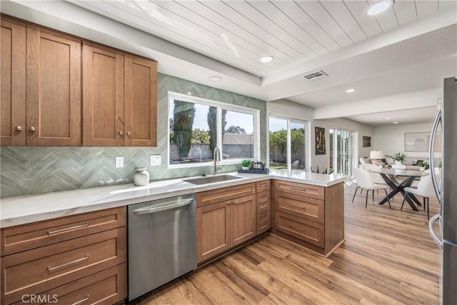 kitchen featuring light wood-style flooring, stainless steel appliances, a peninsula, a sink, and visible vents