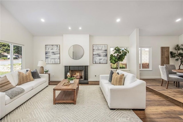 living area featuring a warm lit fireplace, baseboards, wood finished floors, and recessed lighting