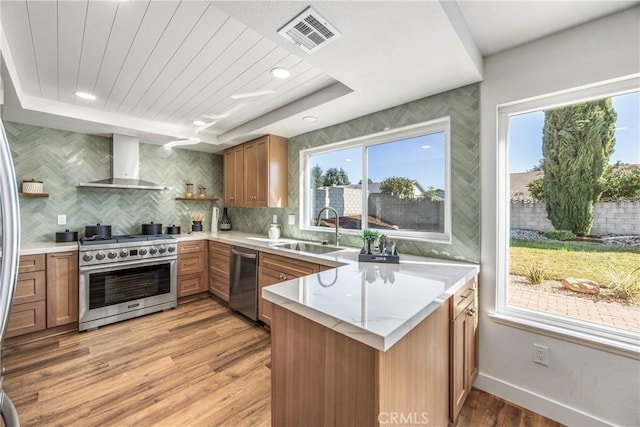 kitchen with visible vents, appliances with stainless steel finishes, a sink, a peninsula, and wall chimney exhaust hood