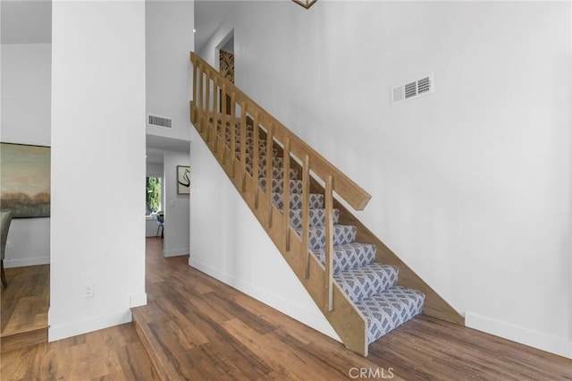 stairs with baseboards, a high ceiling, visible vents, and wood finished floors