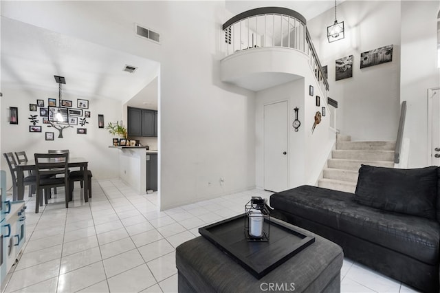 living area featuring stairs, light tile patterned flooring, a towering ceiling, and visible vents