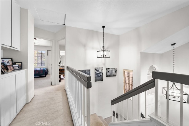 hall featuring light colored carpet, a notable chandelier, and an upstairs landing