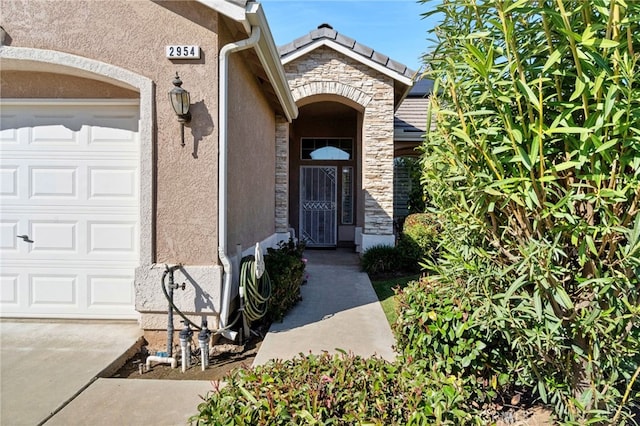 entrance to property with stone siding, an attached garage, and stucco siding