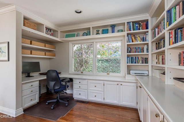 office space featuring ornamental molding, built in desk, and dark wood-type flooring