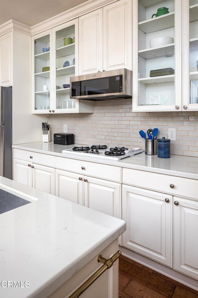 kitchen with tasteful backsplash, light countertops, appliances with stainless steel finishes, glass insert cabinets, and white cabinetry