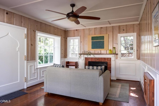 living area featuring a brick fireplace, ceiling fan, dark wood-style flooring, and crown molding