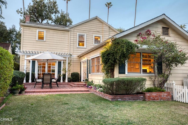 back of property with a patio, a lawn, a chimney, and fence