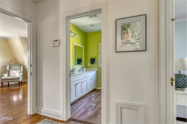 hallway featuring baseboards, wood finished floors, and ornamental molding