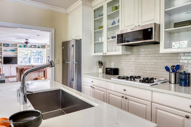 kitchen featuring stainless steel appliances, a sink, white cabinetry, light countertops, and glass insert cabinets