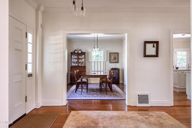 foyer with a chandelier, wood finished floors, visible vents, baseboards, and crown molding