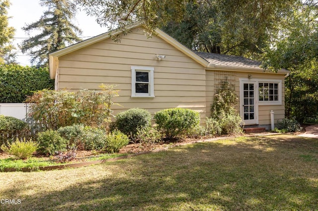 view of home's exterior with entry steps, a shingled roof, a lawn, and fence