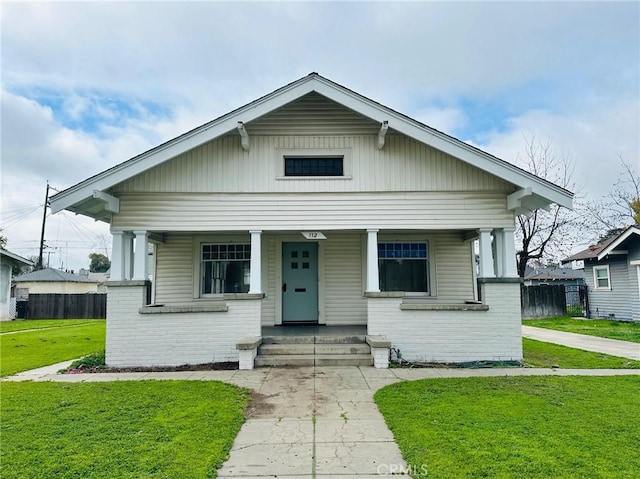 bungalow with brick siding, a porch, a front yard, and fence