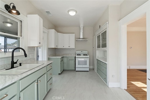 kitchen featuring white gas stove, a sink, light countertops, green cabinets, and wall chimney range hood