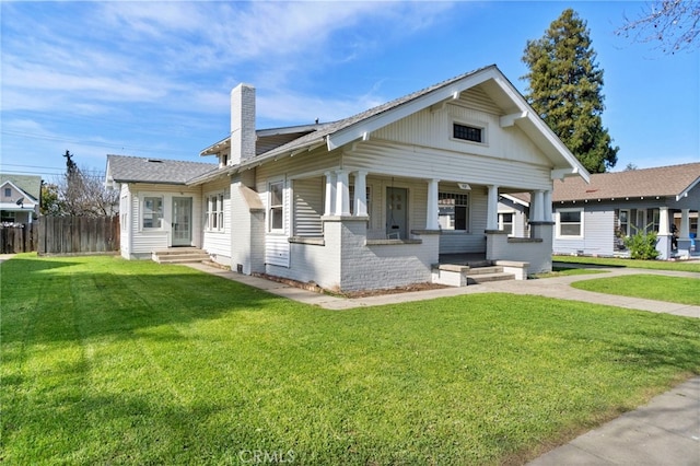 bungalow-style house with brick siding, a front lawn, fence, a porch, and a chimney