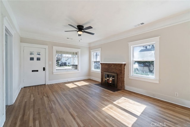 unfurnished living room with visible vents, a brick fireplace, wood finished floors, and ornamental molding