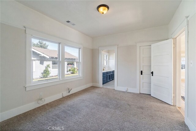 unfurnished bedroom featuring visible vents, light carpet, baseboards, and ensuite bath