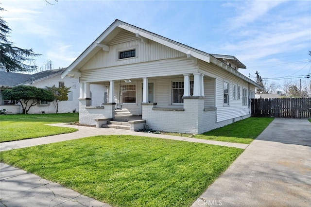 view of front facade featuring a porch, fence, brick siding, and a front yard