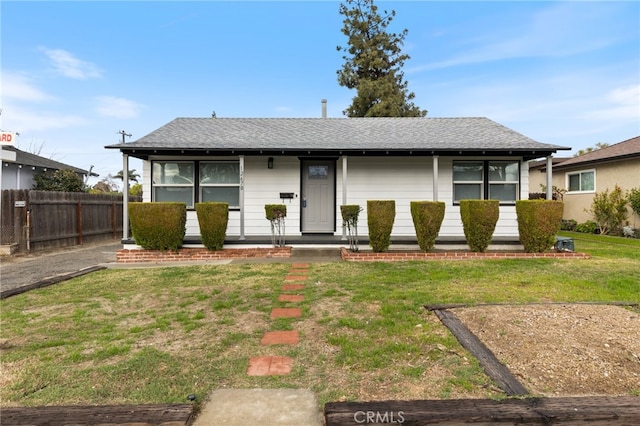 view of front of house featuring covered porch, a shingled roof, a front yard, and fence