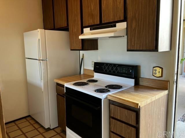 kitchen with light countertops, range with electric cooktop, freestanding refrigerator, and under cabinet range hood