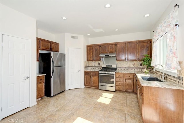 kitchen with under cabinet range hood, stainless steel appliances, a sink, visible vents, and decorative backsplash