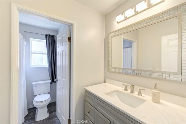 bathroom with toilet, wood finished floors, vanity, and baseboards