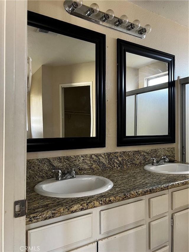 bathroom featuring a textured wall, a sink, and double vanity