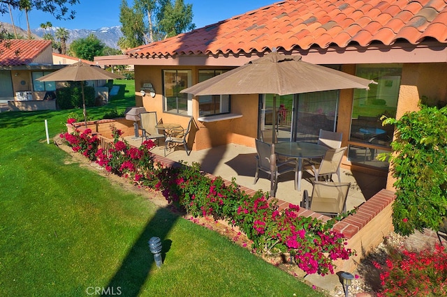 back of property with a tile roof, a yard, stucco siding, a patio area, and a mountain view