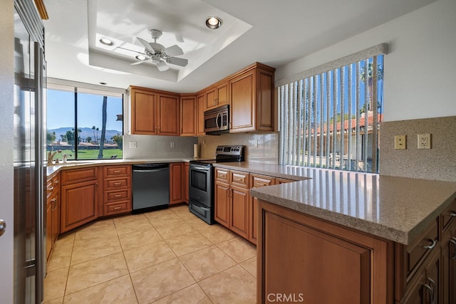 kitchen featuring a raised ceiling, brown cabinets, a peninsula, stainless steel appliances, and a mountain view