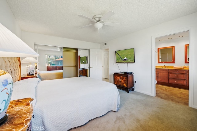 bedroom featuring a textured ceiling, light colored carpet, a sink, visible vents, and ensuite bath