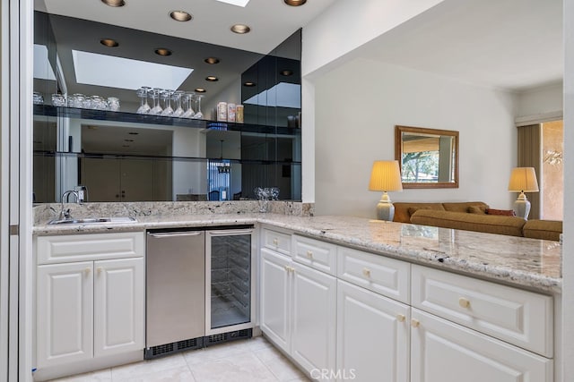 kitchen with light stone countertops, wine cooler, white cabinets, and a sink