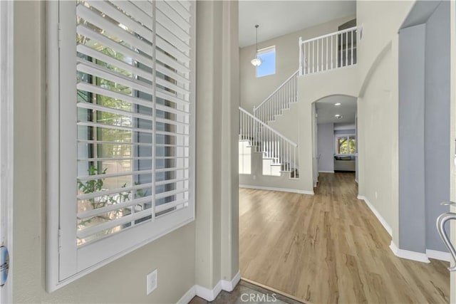 foyer entrance featuring arched walkways, a high ceiling, wood finished floors, baseboards, and stairs