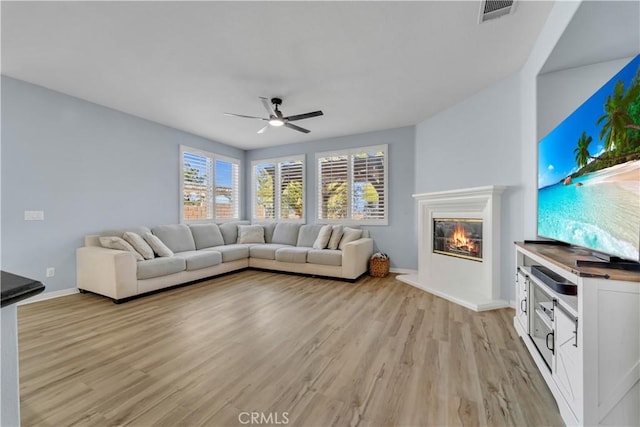 unfurnished living room with light wood-style flooring, visible vents, a ceiling fan, and a glass covered fireplace