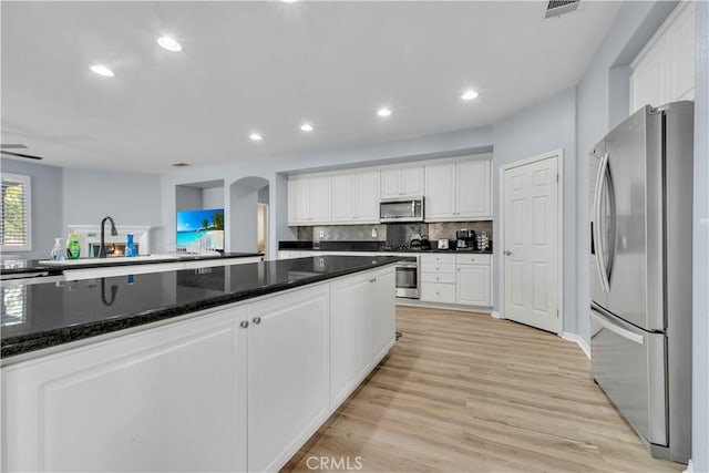 kitchen with stainless steel appliances, arched walkways, light wood-type flooring, and white cabinets