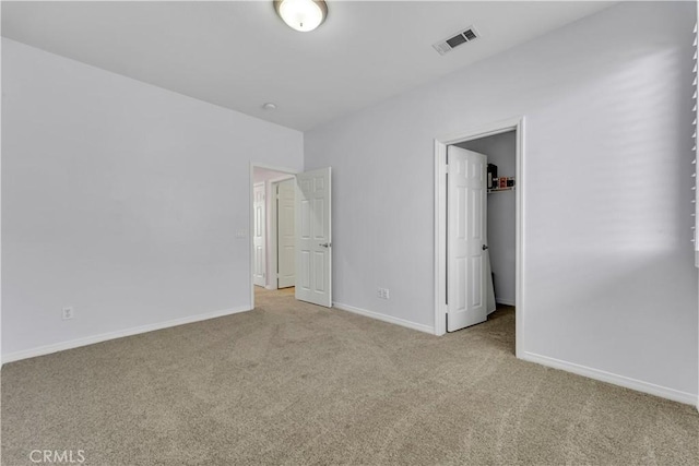 unfurnished bedroom featuring baseboards, a spacious closet, visible vents, and light colored carpet