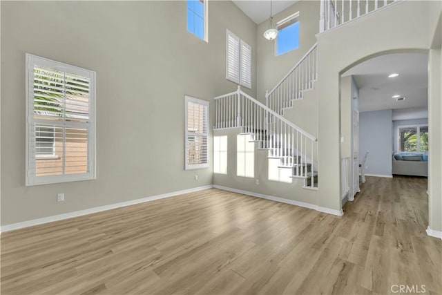 unfurnished living room featuring light wood-style floors, arched walkways, baseboards, and stairs