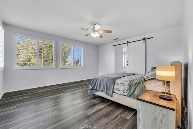 bedroom with a barn door, visible vents, baseboards, dark wood-style floors, and ceiling fan