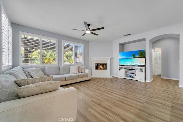 living area featuring baseboards, visible vents, arched walkways, a glass covered fireplace, and light wood-style floors