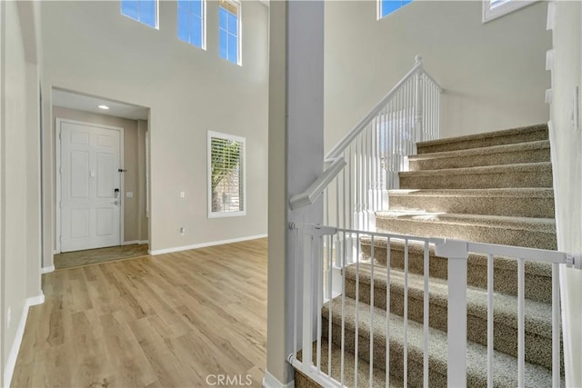 stairway featuring wood finished floors, a towering ceiling, and baseboards