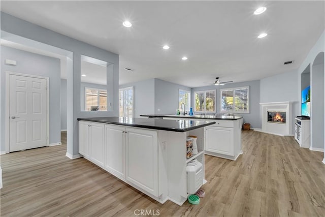 kitchen featuring dark countertops, a glass covered fireplace, white cabinetry, light wood-type flooring, and a peninsula